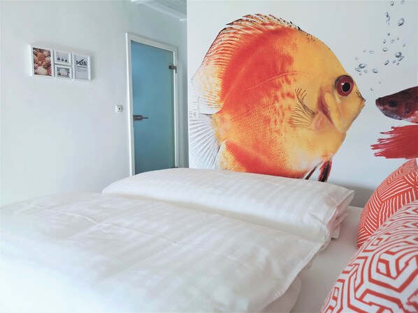 Une pièce avec un lit, un mur décoré d’une fresque représentant des poissons et une porte.