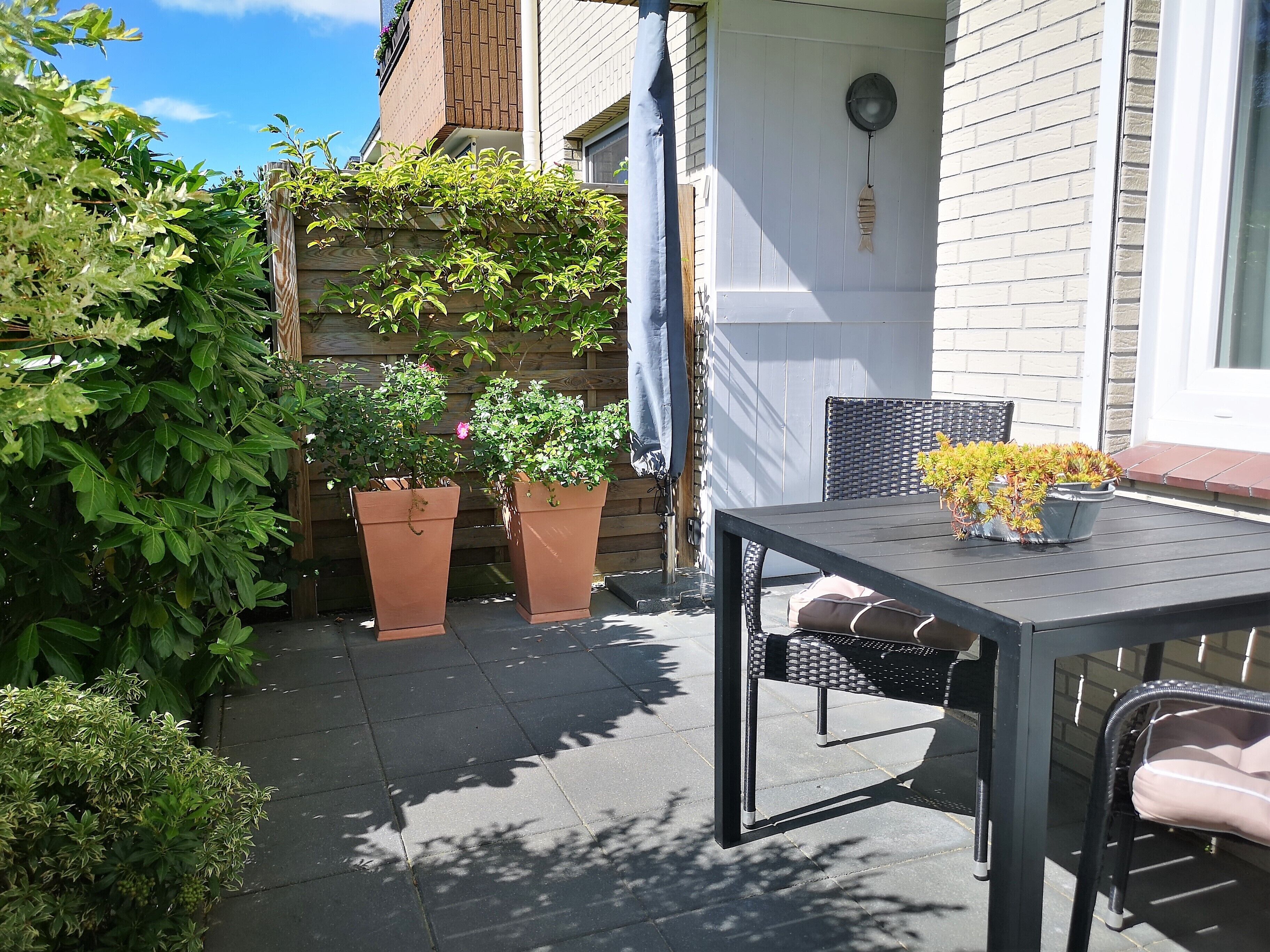 A patio with a table and chairs, surrounded by potted plants and a wooden fence.