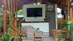 A covered outdoor seating area with a flat-screen TV, wooden furniture, and potted plants. - Kerusso Haven (Puerto Princesa)