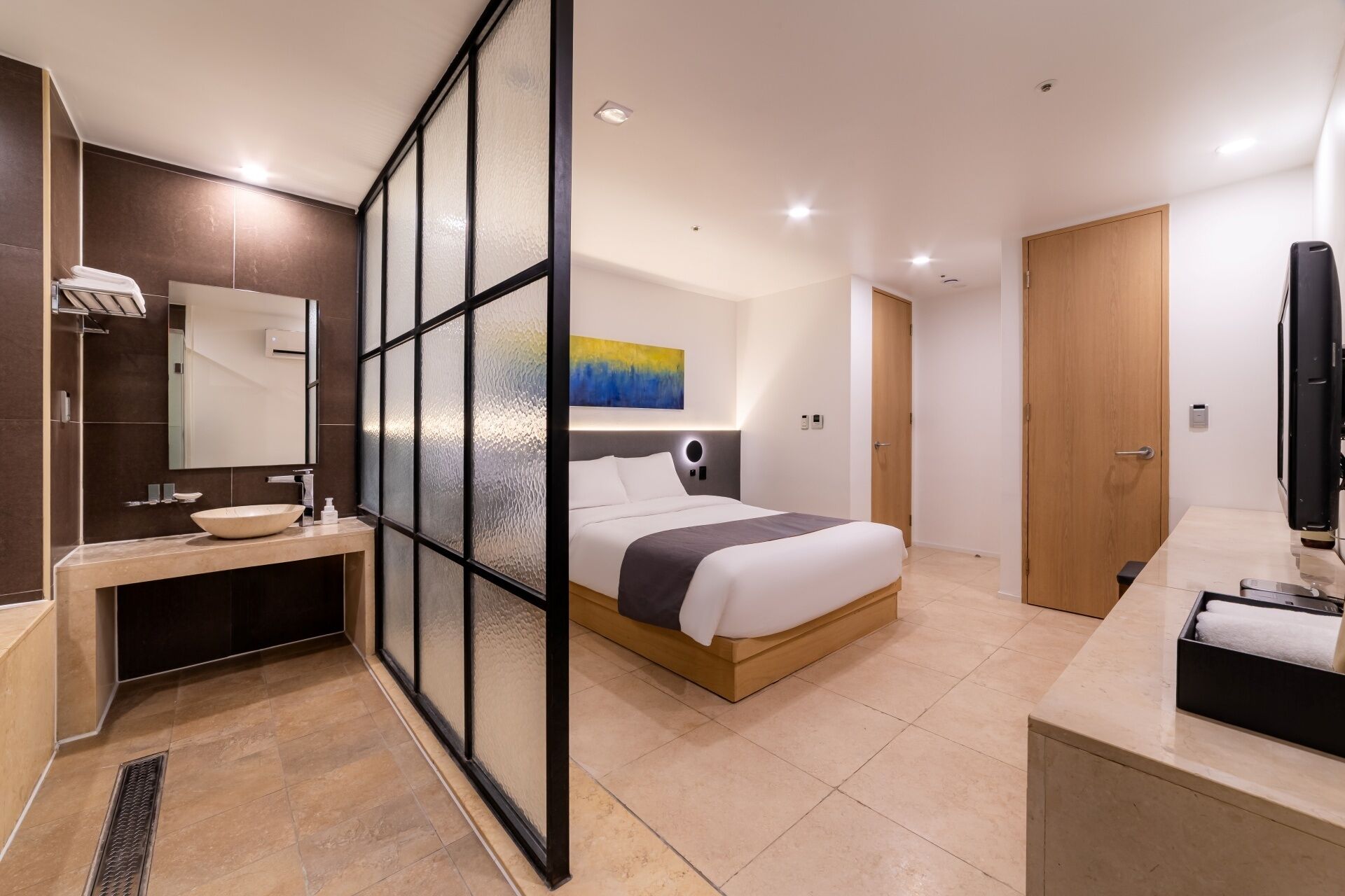 Una habitación de hotel moderna con una cama, un baño con lavabo y espejo, y un televisor.