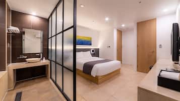 Una habitación de hotel moderna con una cama, un baño con lavabo y espejo, y un televisor.