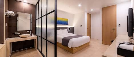 A modern hotel room with a bed, a bathroom with a sink and mirror, and a television.