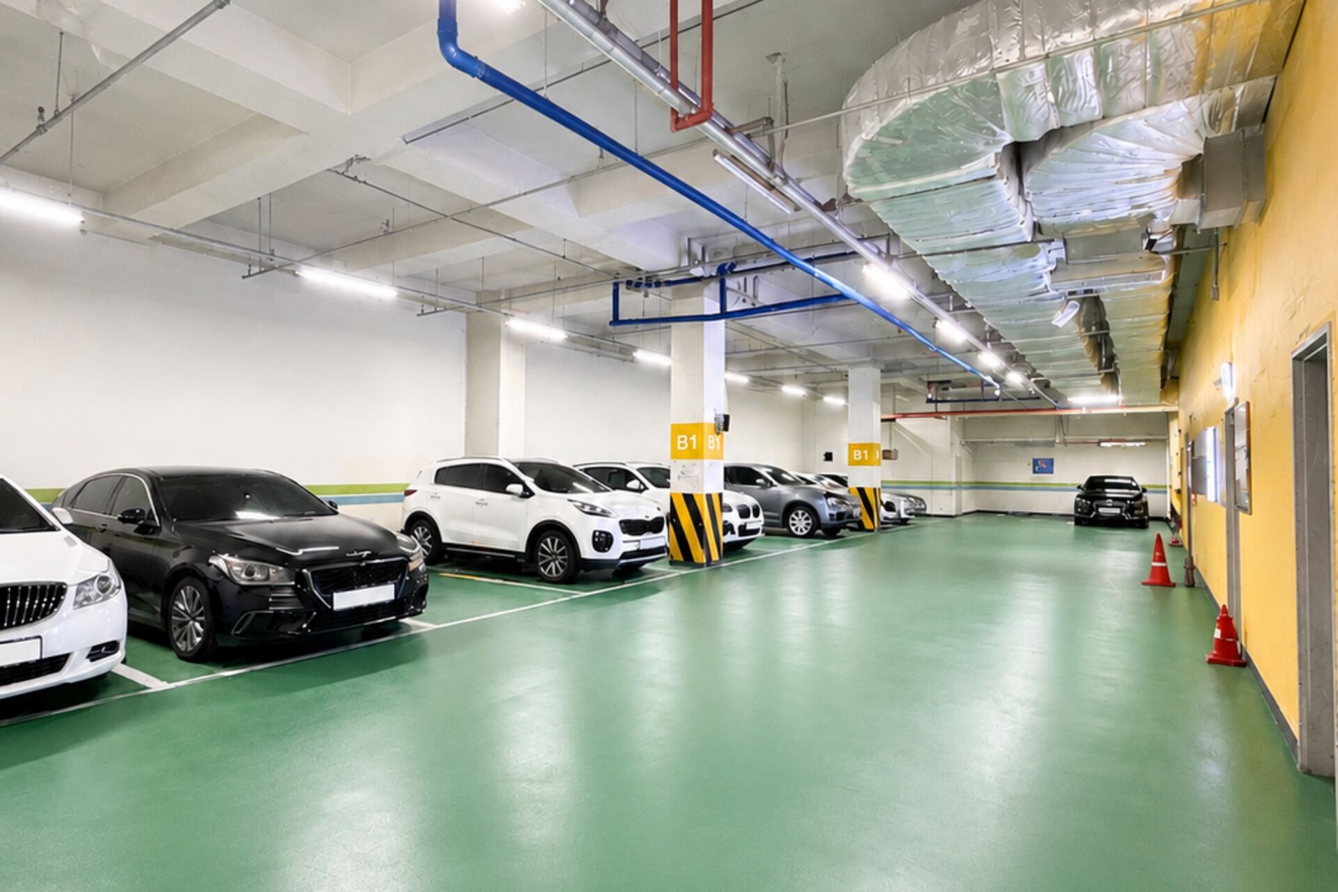 Un estacionamiento con varias filas de coches aparcados, señalización clara y suelo verde.