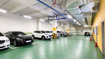 Un estacionamiento con varias filas de coches aparcados, señalización clara y suelo verde.