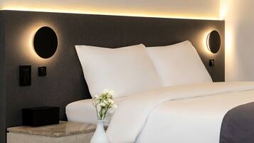 Una habitación de hotel moderna con una cama grande, una mesita de noche, un florero con flores e iluminación en la pared.
