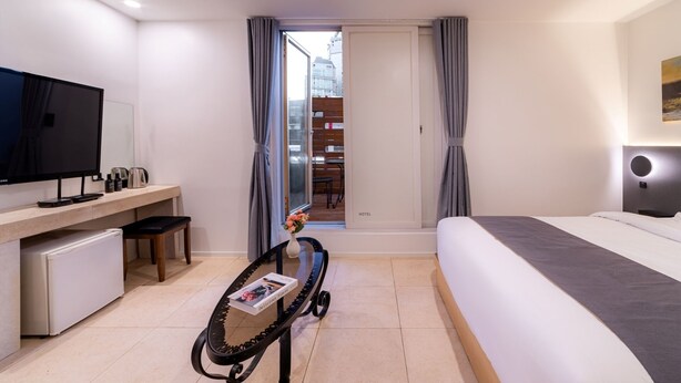 Habitación de hotel con cama, escritorio con televisor, refrigerador pequeño y vista al exterior.
