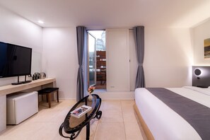 Quarto de hotel com cama, escrivaninha com televisão, mini-geladeira e vista para o exterior.