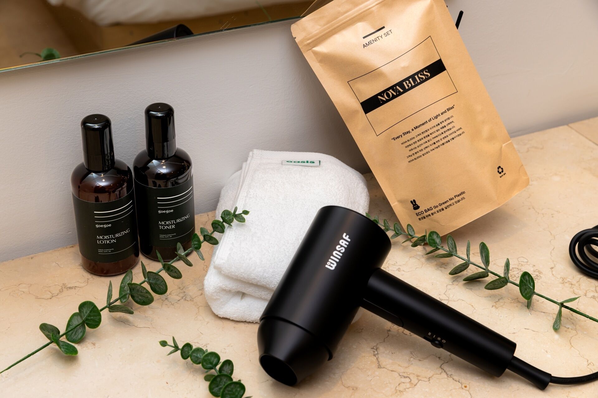 A bathroom with a hairdryer, two bottles of lotion, a towel, and a bag labeled 'NOVA BLISS.'