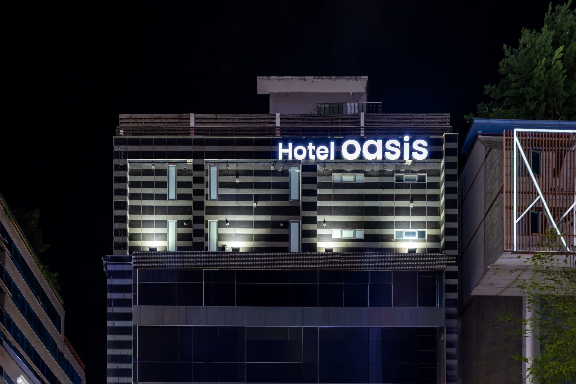 A modern hotel building with a prominent sign reading 'Hotel Oasis' at night.