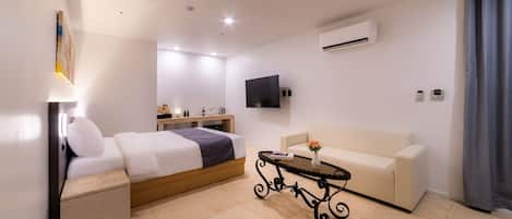 Una camera d'albergo moderna con un letto, un divano, un tavolino, una TV e un condizionatore d'aria.