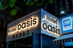 A hotel sign with illuminated letters spelling 'Hotel Oasis' and a smaller sign indicating 'Takara Tommy A.R.T.S' since 1986.