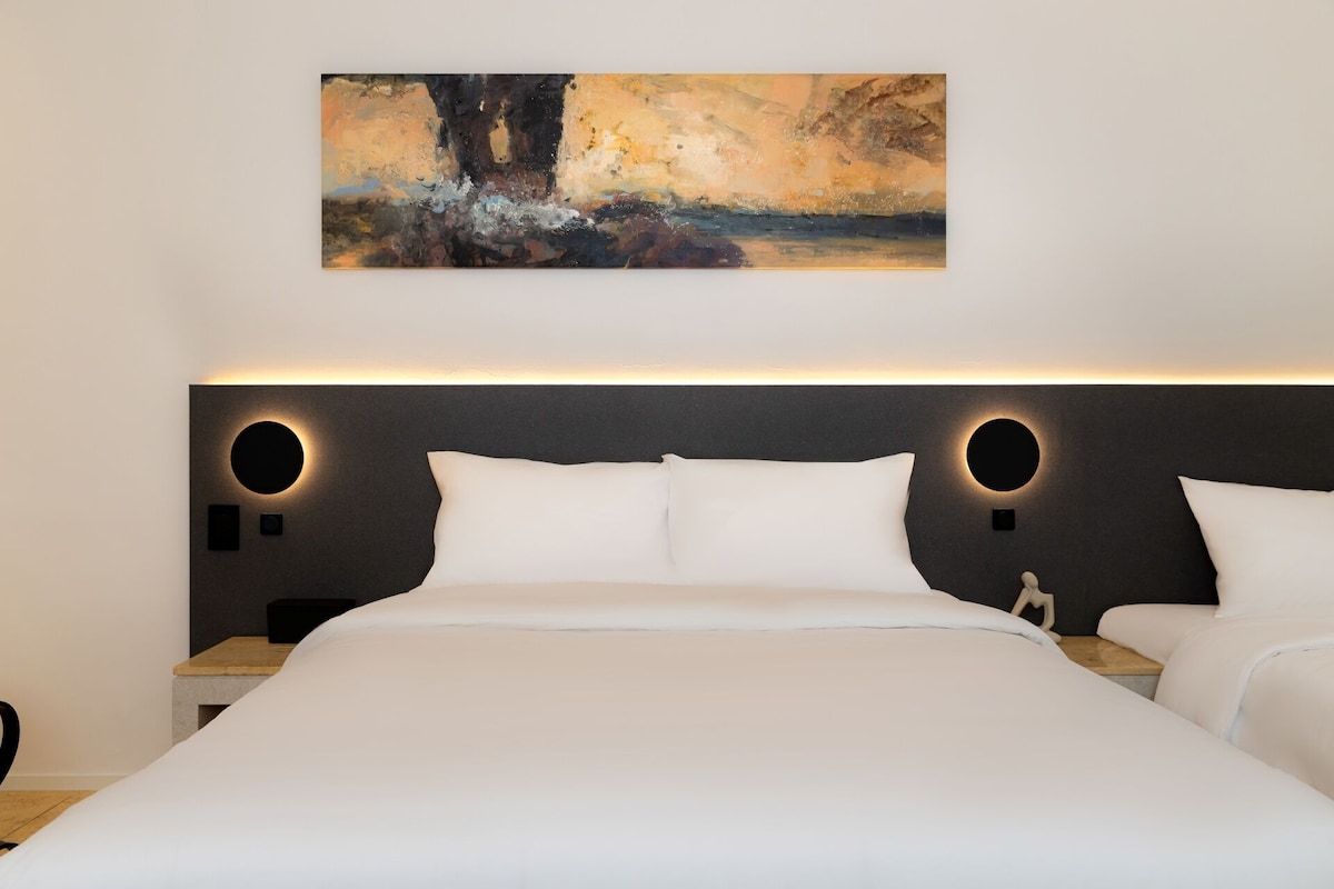 A modern hotel room with a large bed, two bedside tables, and a painting on the wall.