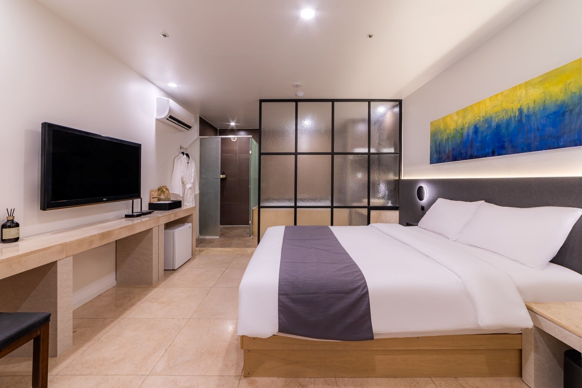 Quarto de hotel com cama, televisão, secretária, chuveiro e banheiro.