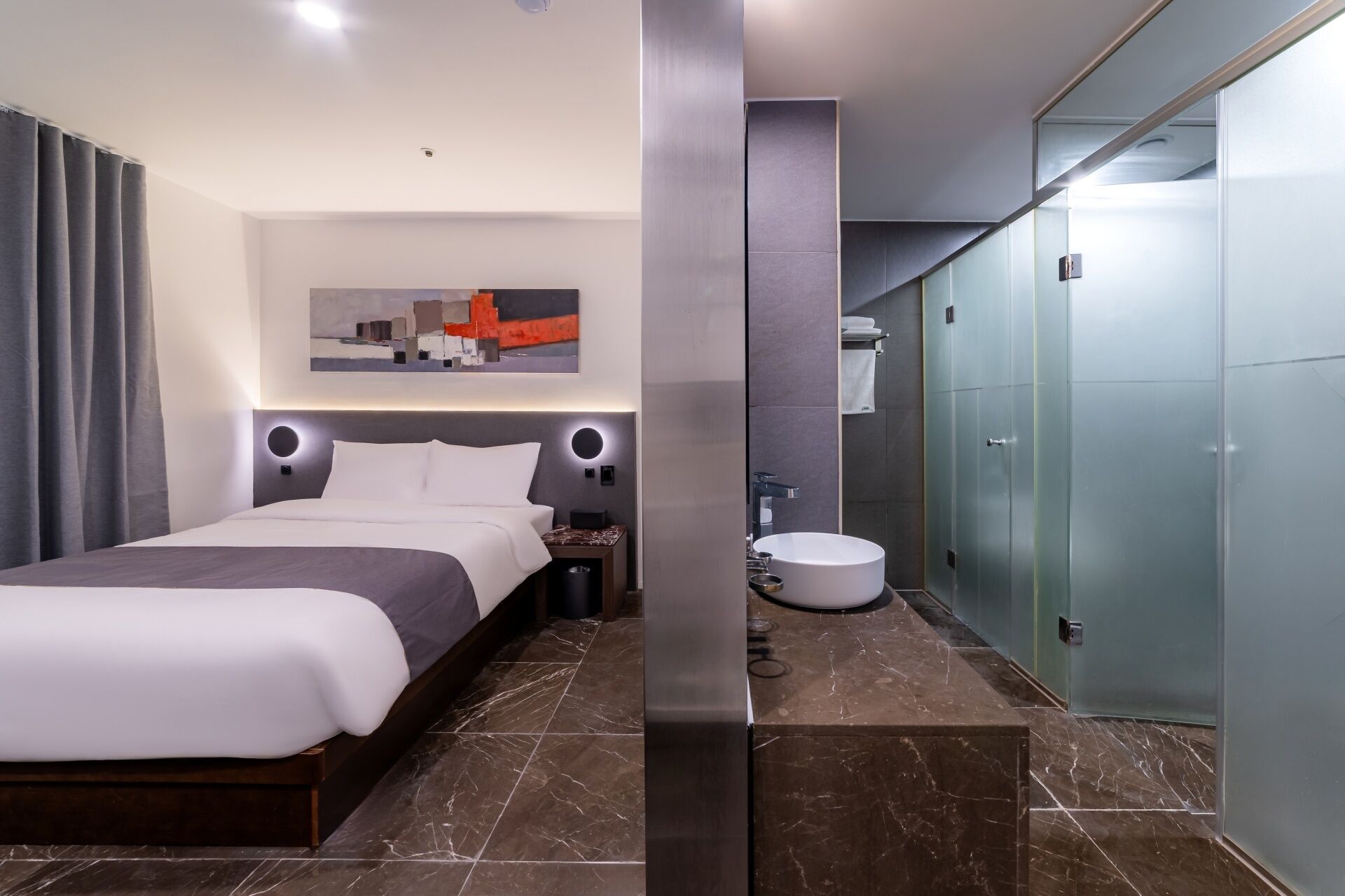 Una habitación de hotel moderna con una cama grande, un baño con un lavabo redondo y un armario.