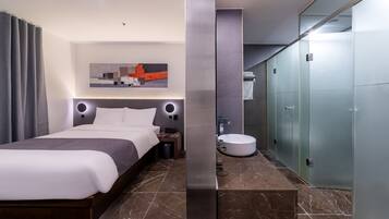 Una habitación de hotel moderna con una cama grande, un baño con un lavabo redondo y un armario.