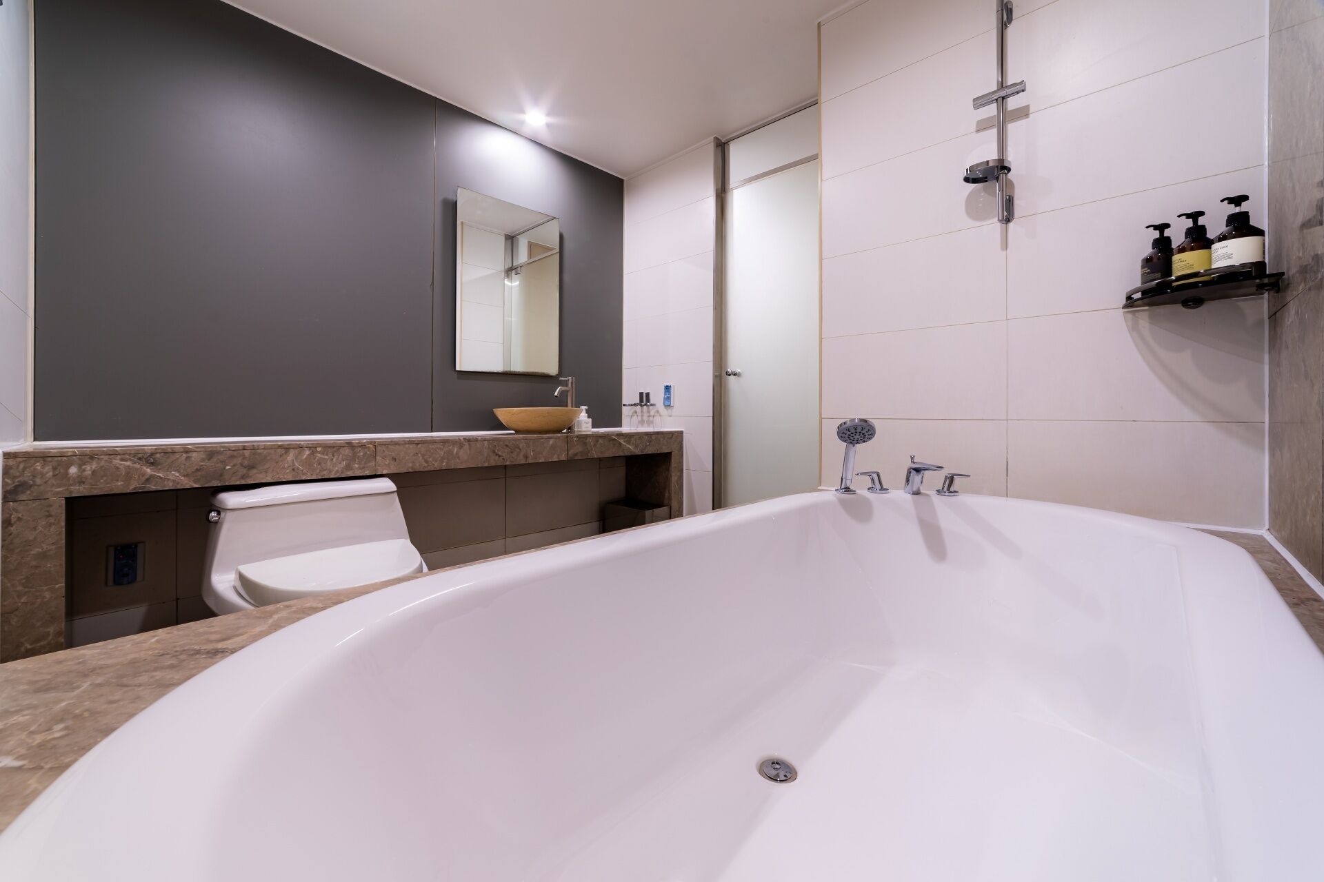 A modern bathroom with a large bathtub, a toilet, and a sink with a mirror above.