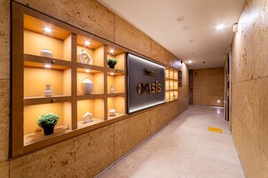 Zona de recepción de un hotel con diseño moderno, que incluye un mostrador de recepción, un letrero en la pared y jarrones decorativos.