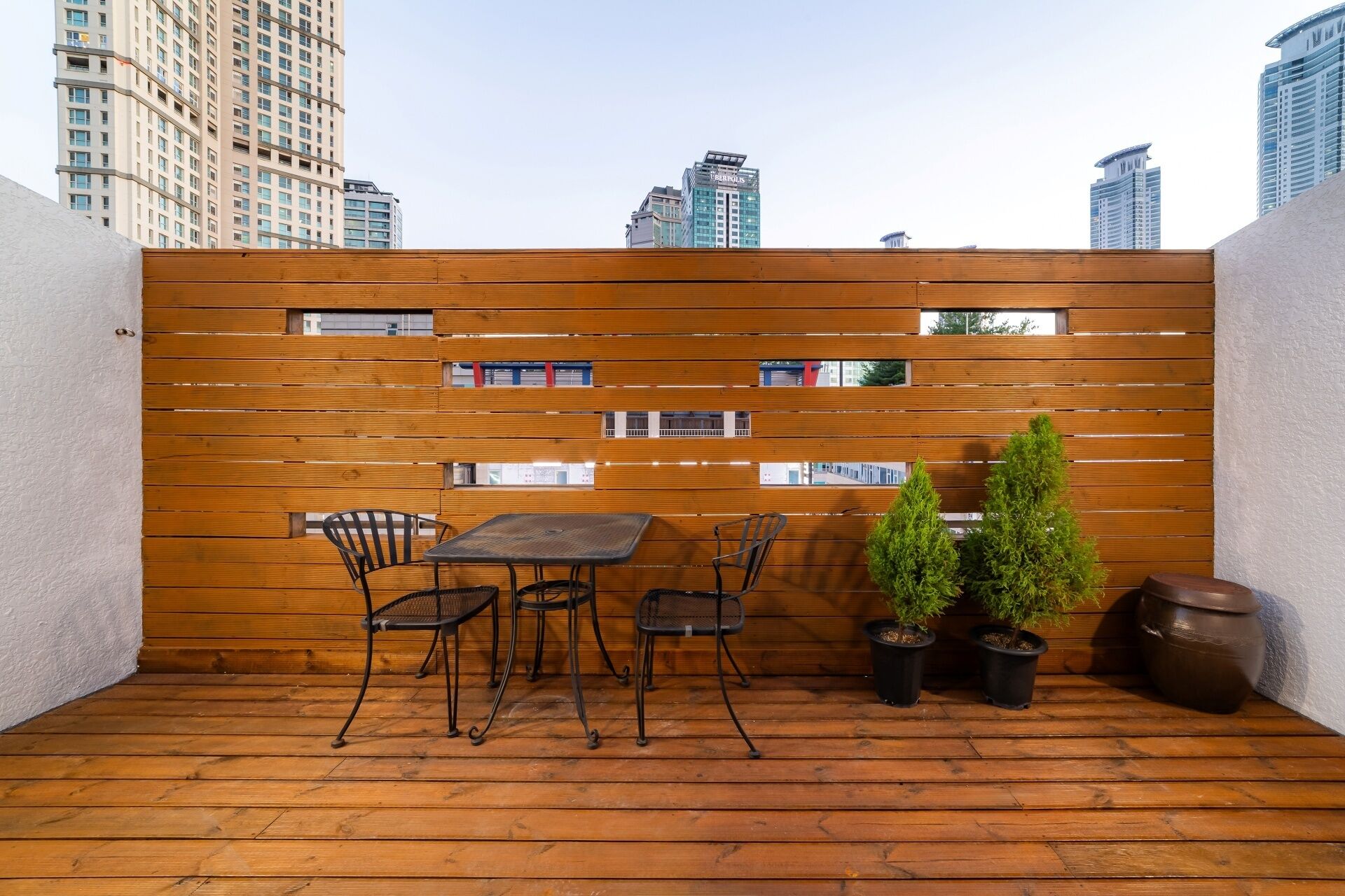 Une terrasse en bois avec une table et des chaises, des plantes en pot et une vue sur les bâtiments de la ville.