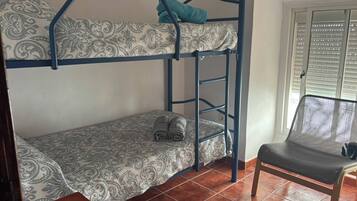 A bunk bed with patterned bedding, a chair with a mesh backrest, and a window with blinds.