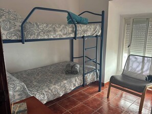 A bunk bed with patterned bedding, a chair with a mesh backrest, and a window with blinds.