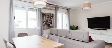 Una sala de estar moderna con una mesa de comedor de madera, un sofá gris y un televisor de pantalla plana montado en la pared.