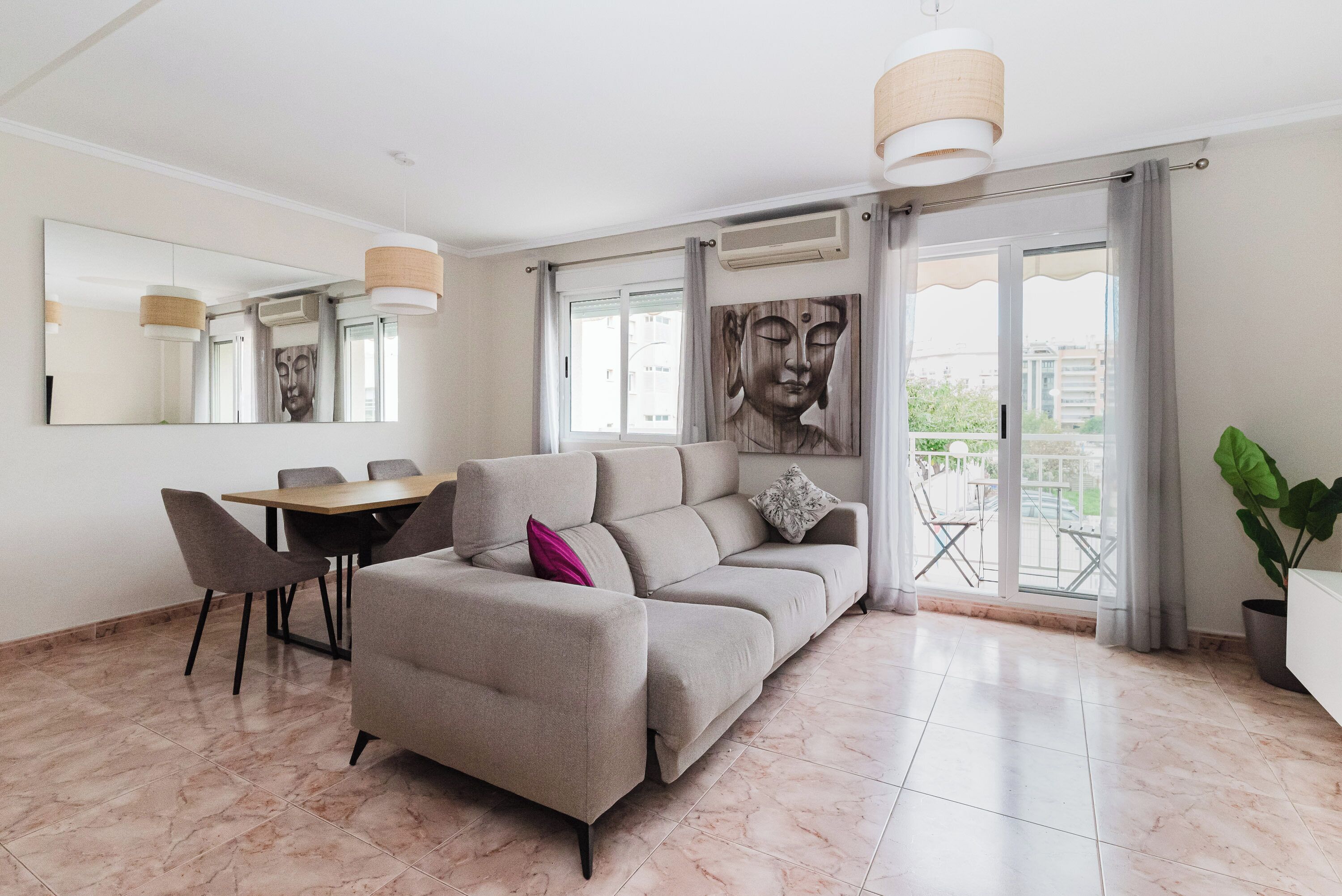 A modern living room with a sofa, a dining table, chairs, and a large window with a view.