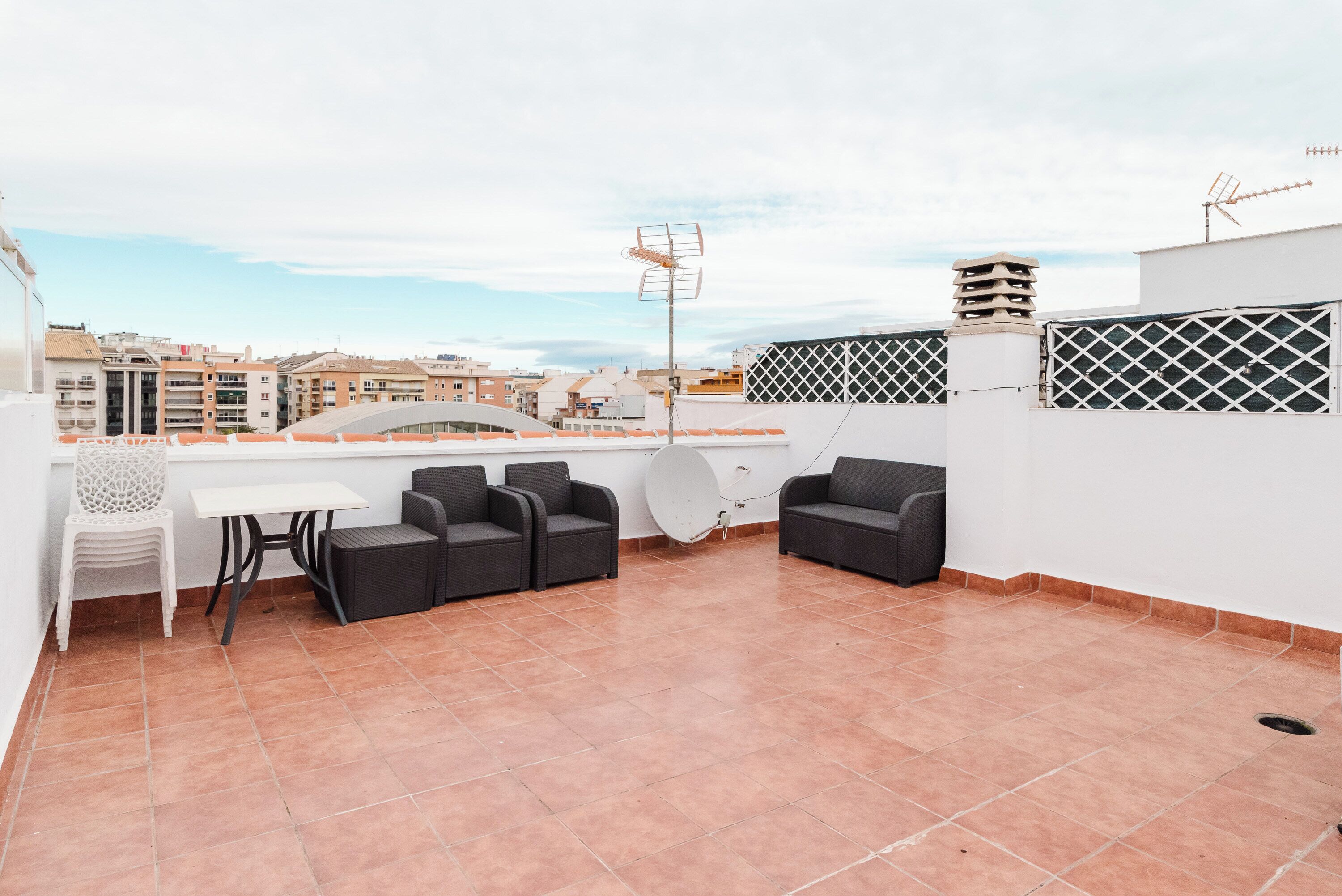 A rooftop terrace with a table and chairs, a TV antenna, and a view of the cityscape.