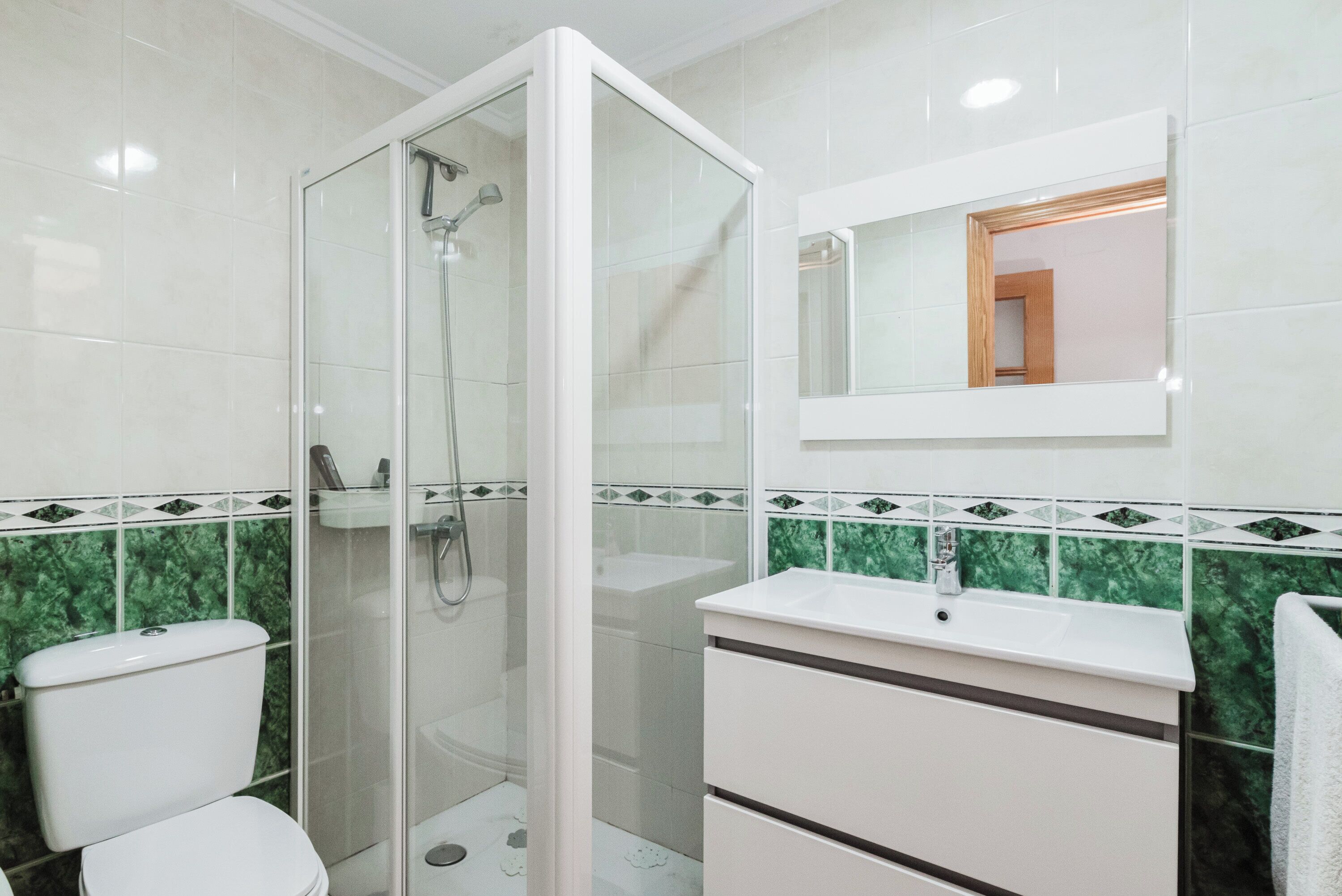 Un baño con ducha de vidrio, un lavabo blanco y un espejo sobre el lavabo.