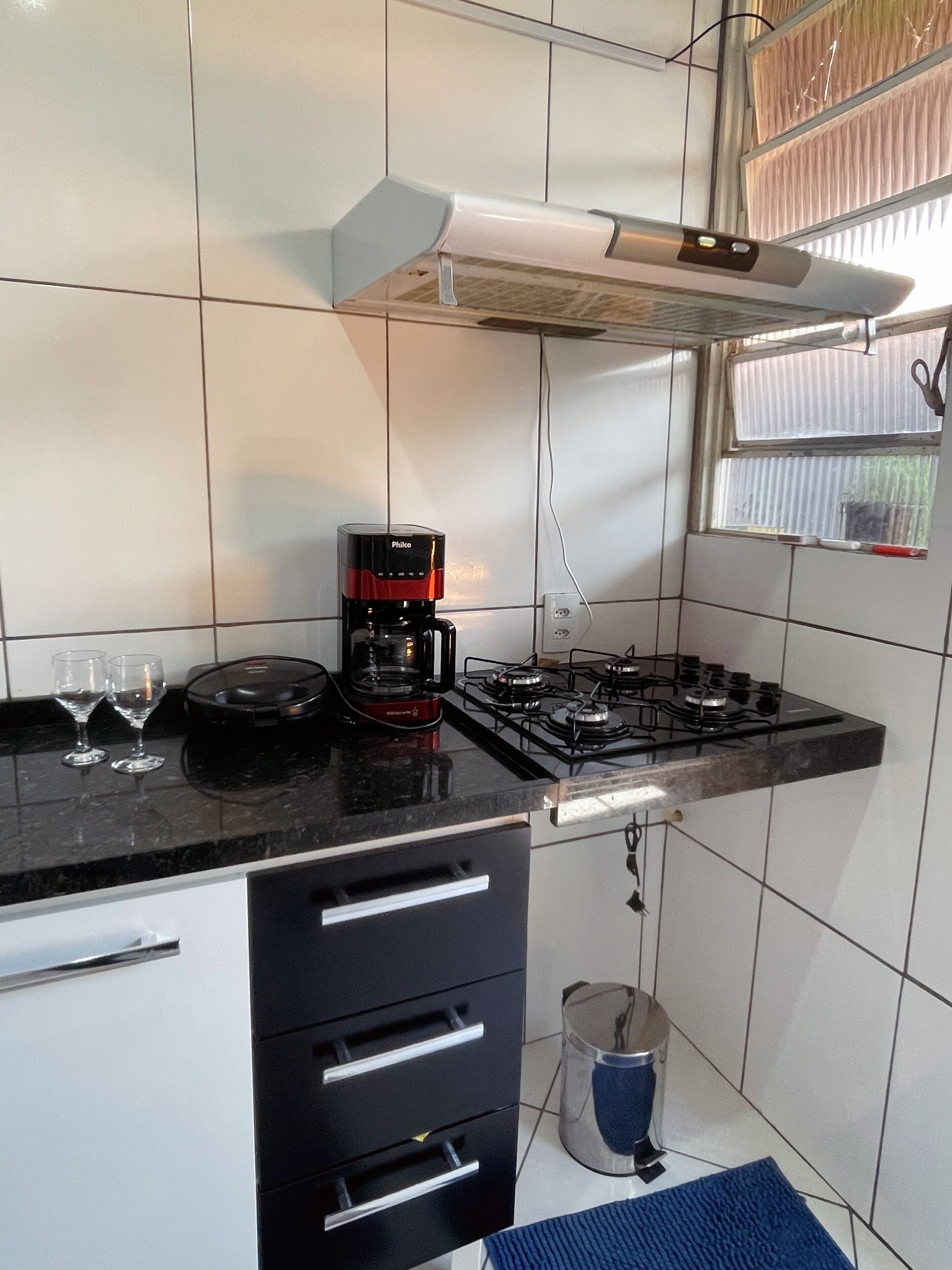A kitchen with a gas stove, a coffee maker, and a window with blinds.