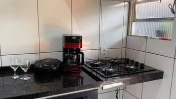 A kitchen with a gas stove, a coffee maker, and a window with blinds.
