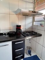 Una cocina con estufa a gas, cafetera y ventana con persianas.