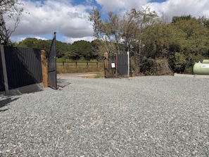 A gravel driveway leading to a gated entrance with a wooden fence and a metal gate.