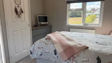Un dormitorio con cama, televisor sobre una cómoda, ventana con vistas al exterior y un atrapasueños en la pared.