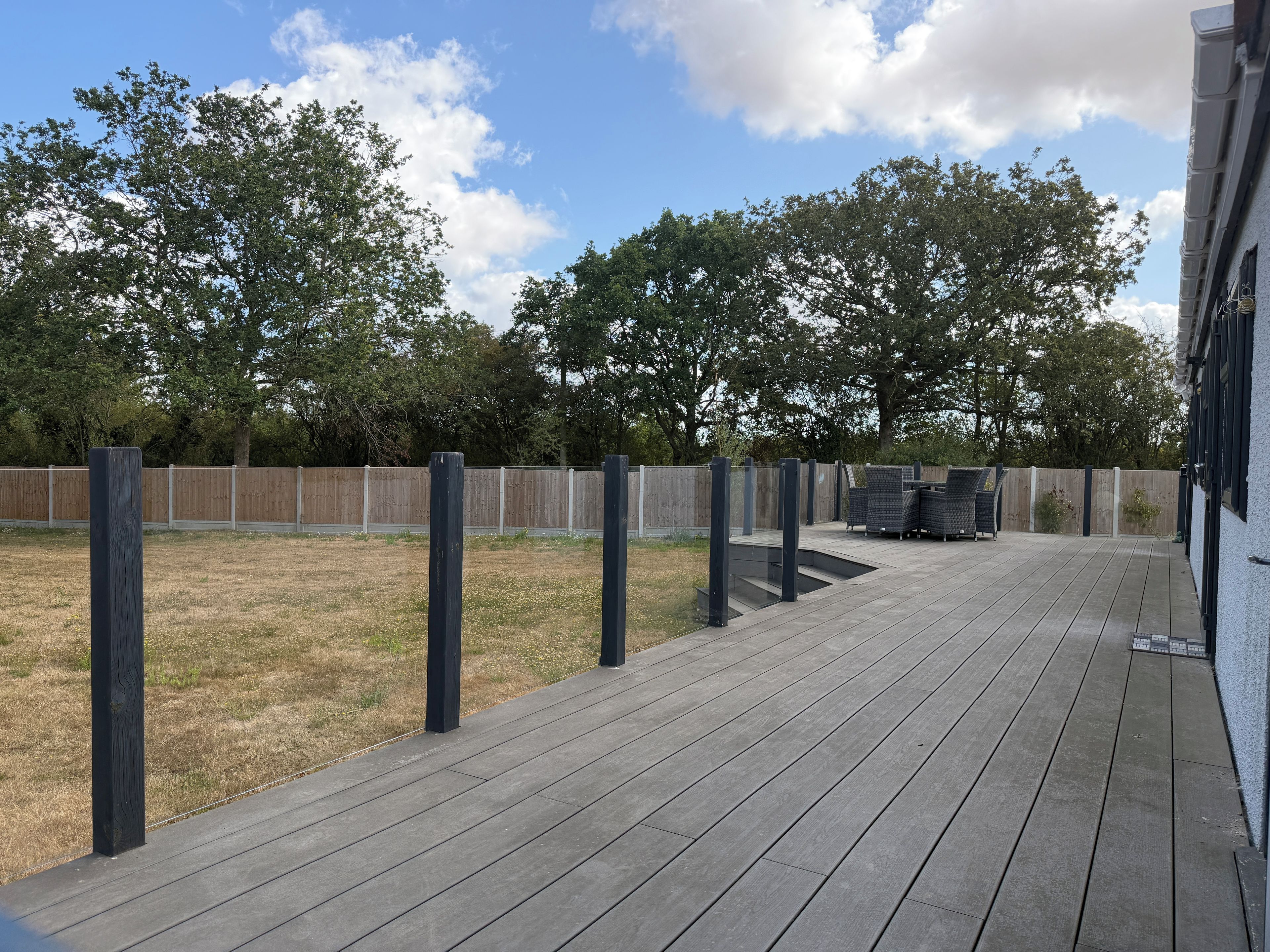 A deck with a wooden floor and black posts, a fenced yard, and a building with a white exterior.