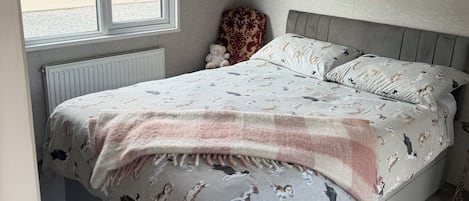 Un dormitorio con cama, ventana, radiador y un osito de peluche.