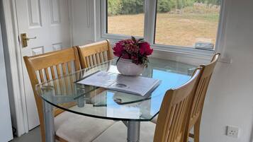 A dining area with a glass table surrounded by wooden chairs, a vase with flowers, and a view of the outdoors through a window.