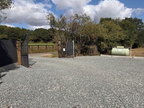 A gravel parking area with a gated entrance, a green cylindrical tank, and a wooden fence.
