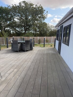A wooden deck with outdoor furniture, a white building with windows, and a wooden fence.
