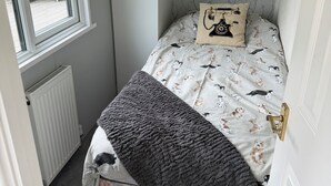 Um quarto pequeno com uma cama de solteiro, uma janela, um radiador e uma porta.