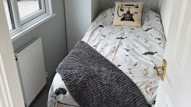 A small bedroom with a single bed, a window, a radiator, and a door.