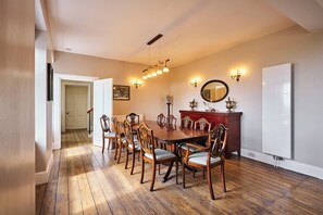 Ein Esszimmer mit einem großen Holztisch, umgeben von Stühlen, einer Kristallleuchter und Wandleuchten.