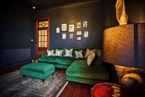 Ein Zimmer mit einer grünen Sofagarnitur, einem gemusterten Teppich und einer Wand mit gerahmten Bildern.