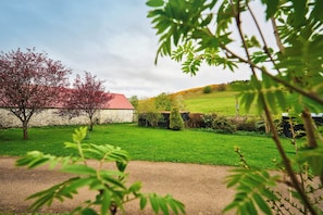 Ländliche Landschaft mit einem Steingebäude, einem Baum mit roten Blättern und einem grünen Feld.