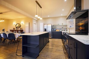 A modern kitchen with a central island, dark cabinetry, and a dining area with a table set for four. - Kinclune House Luxury Estate Mansion, Angus Glens (Kirkton of Kingoldrum)