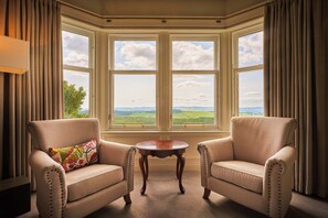 Quarto com duas poltronas voltadas para uma janela panorâmica com vista para a paisagem.