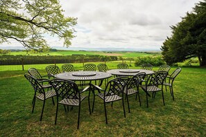 A circular outdoor seating area with metal chairs and tables, surrounded by a grassy field with a view of a distant landscape. - Kinclune House Luxury Estate Mansion, Angus Glens (Kirkton of Kingoldrum)