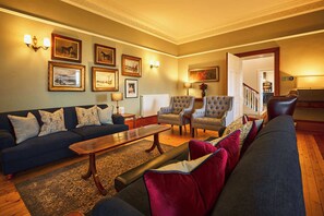A spacious living room with a dark blue sofa, two armchairs, a coffee table, and a patterned rug. - Kinclune House Luxury Estate Mansion, Angus Glens (Kirkton of Kingoldrum)