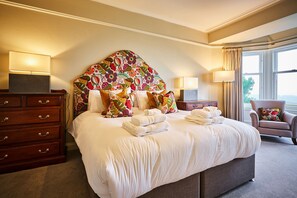 Une chambre d’hôtel avec un grand lit, une commode, une chaise et une fenêtre avec des rideaux.