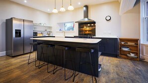 Une cuisine moderne dotée d’un îlot central, de tabourets de bar, d’un réfrigérateur en acier inoxydable, d’un four encastré et de luminaires suspendus.