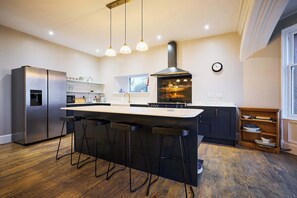 A modern kitchen with a central island, bar stools, a stainless steel refrigerator, a built-in oven, and pendant lighting. - Kinclune House & Annex Luxury Mansion, Angus Glens (Kirkton of Kingoldrum)